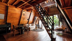 Een houten interieur met een trap, een eethoek en een zithoek met uitzicht op groen.
