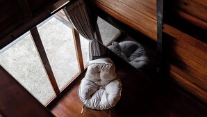 Een kamer met een houten plafond, een raam met uitzicht op een grindpad, en twee comfortabele stoelen.