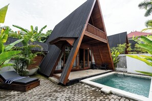 Una casa moderna con piscina, terraza de madera y una tumbona.