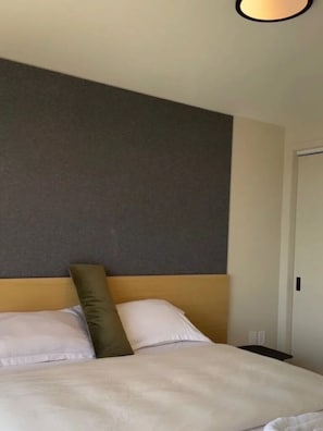 Habitación de hotel con una cama, cabecero, una puerta y una pared con textura.