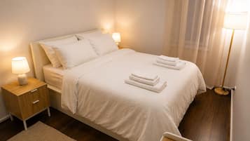 A neatly made bed with white linens, two bedside lamps, a wooden nightstand, and a mirror.