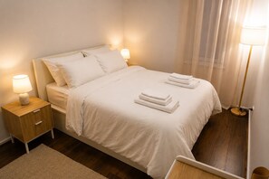 Ein ordentlich bezogenes Bett mit weißen Leinen, zwei Nachttischlampen, ein Holznachttisch und ein Spiegel.