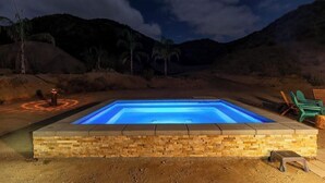 Una piscina rettangolare con bordo in pietra, circondata da un’area in terra con sedie e un piccolo elemento decorativo a fuoco.