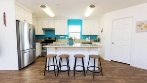 Una cucina moderna con mobili bianchi, frigorifero in acciaio inossidabile, isola centrale con sgabelli e una parete d'accento blu.