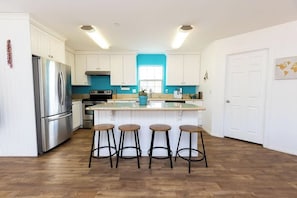 Eine moderne Küche mit weißen Schränken, einem Edelstahl-Kühlschrank, einer zentralen Kochinsel mit Hockern und einer blauen Akzentwand.