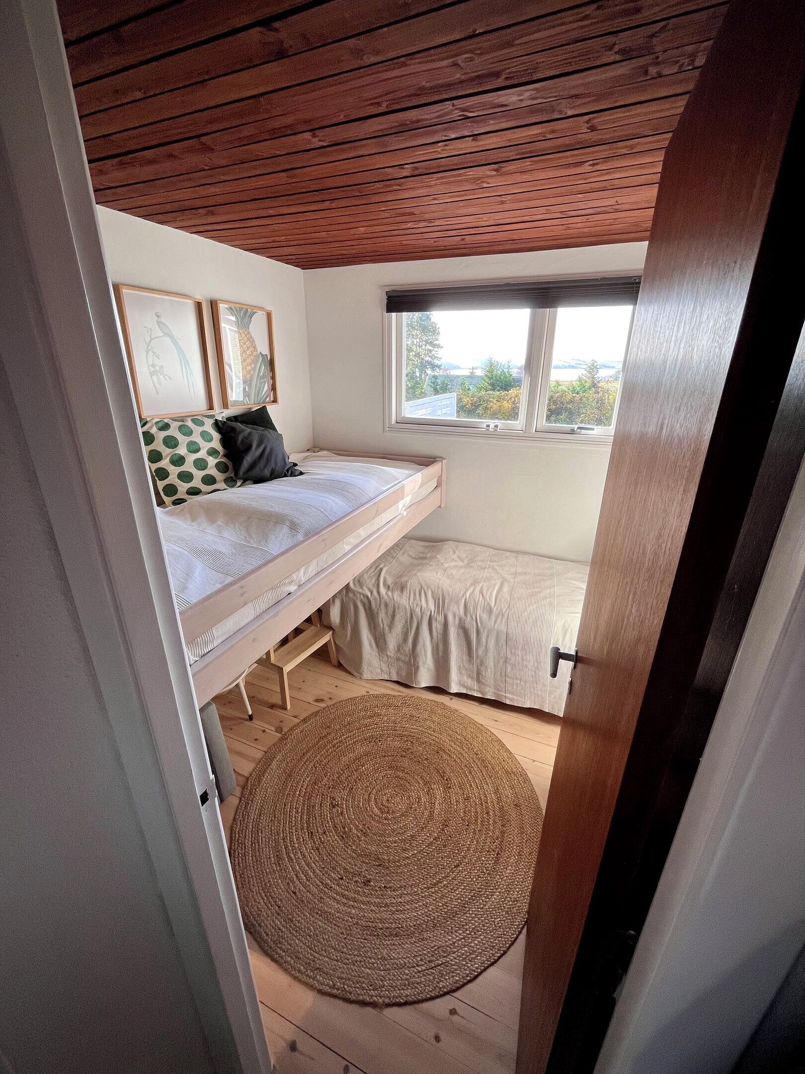 A bedroom with a bunk bed, a window with a view, and a woven rug on the floor.