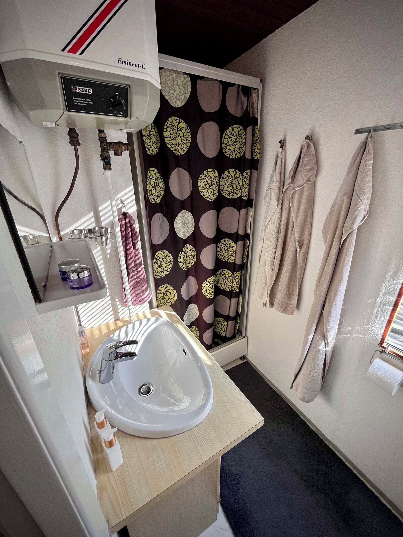 A bathroom with a sink, towel rack, shower curtain, and a control panel labeled 'Eminent-E'.