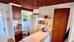 A compact kitchen with wooden cabinets, a white countertop, a hanging light fixture, and a door leading to another room.