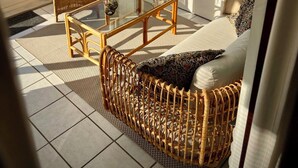 A sunlit room with wicker furniture, a glass coffee table, and a view of the outdoors.
