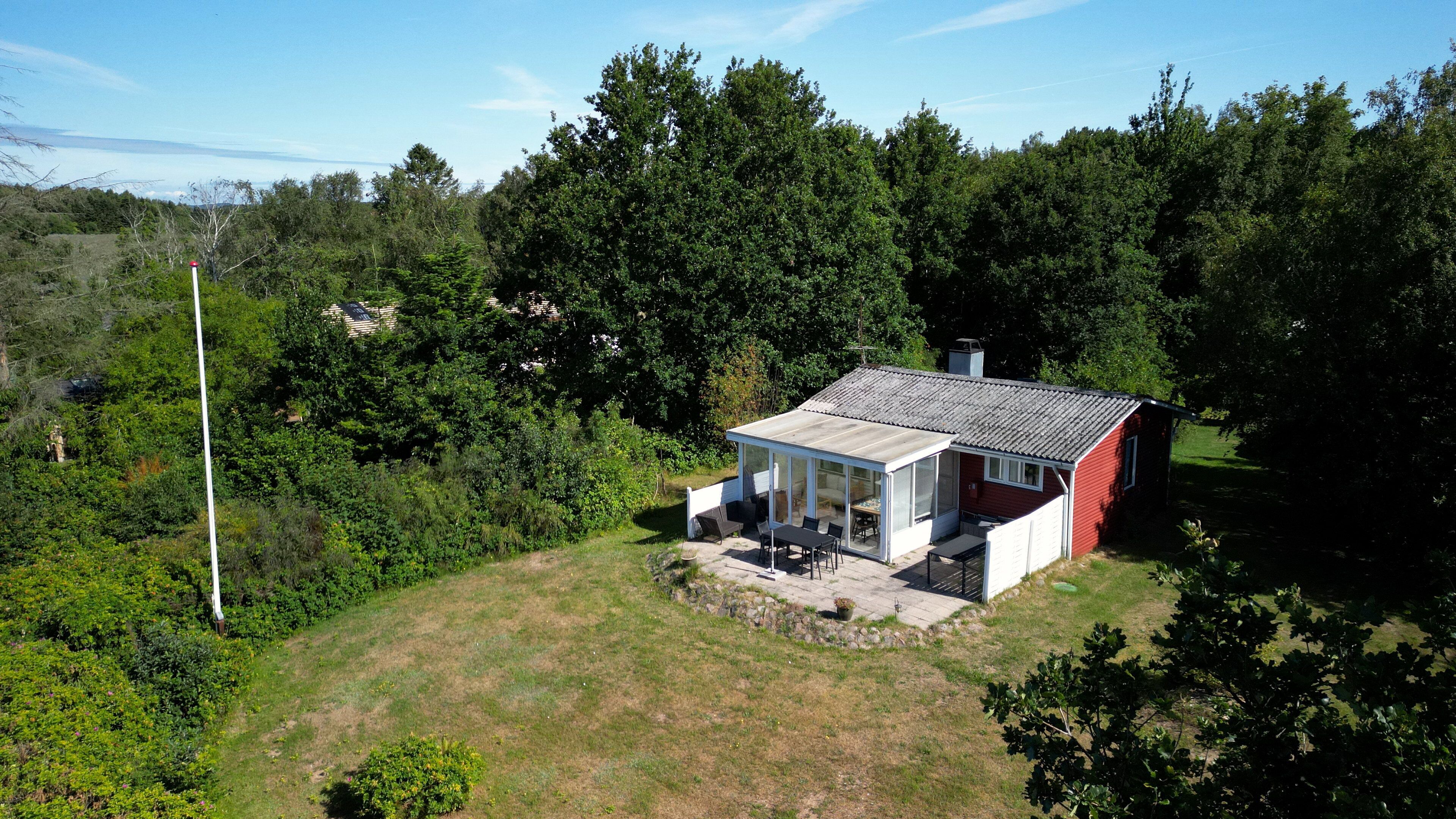 Une maison de plain-pied dotée d’un patio couvert, entourée d’arbres denses et d’une pelouse.