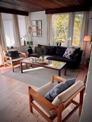 A cozy living room with a sofa, armchairs, a coffee table, and a view of trees through large windows. - 2 bedroom accommodation in Millinge (Millinge)