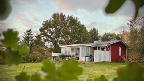 A red cabin with a glass enclosure, surrounded by trees and a grassy area.