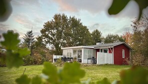 Eine rote Holzhütte mit Glasveranda, umgeben von Bäumen und einer Rasenfläche.