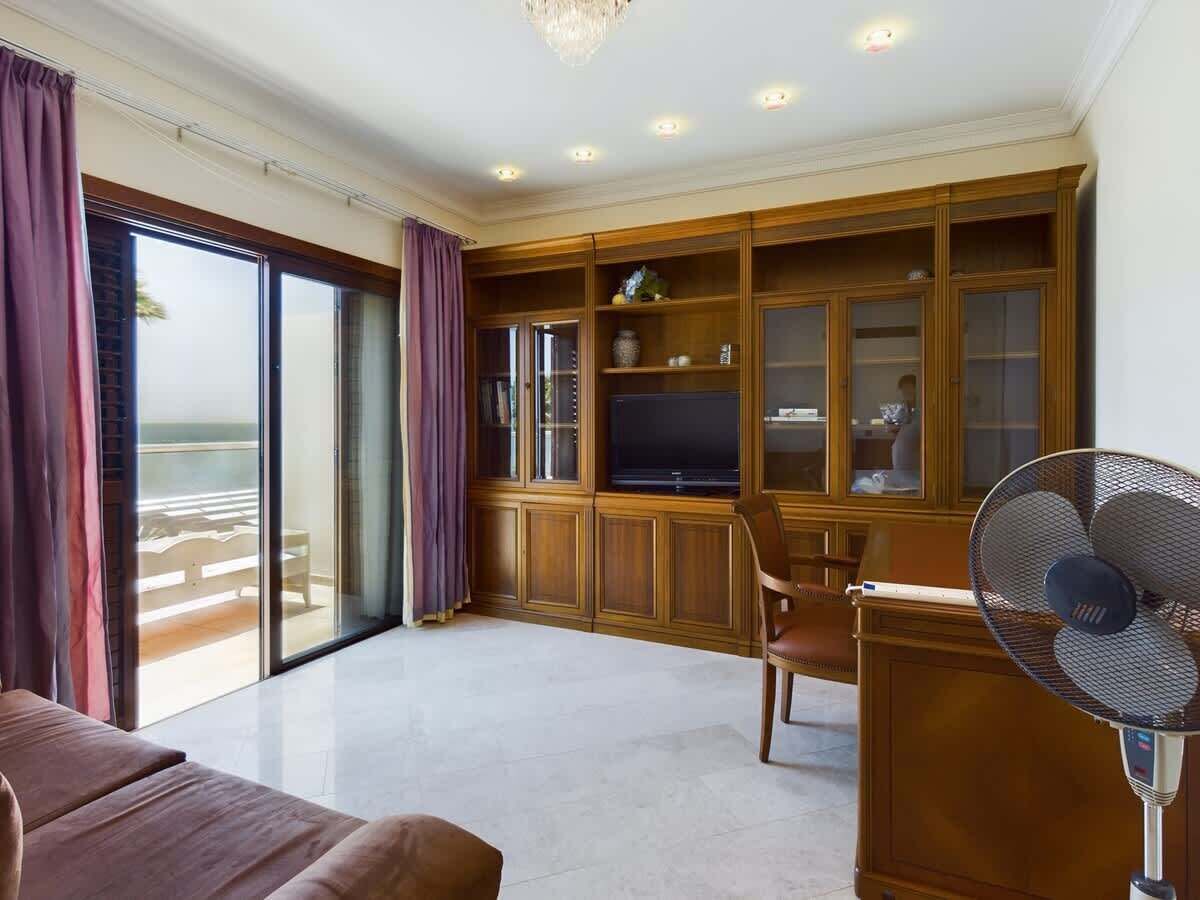 Ein Zimmer mit einer großen Schiebeglaswand, einer Holz-Unterhaltungsanlage, einem Flachbildfernseher, einem Ventilator und einer gepolsterten Sitzecke.