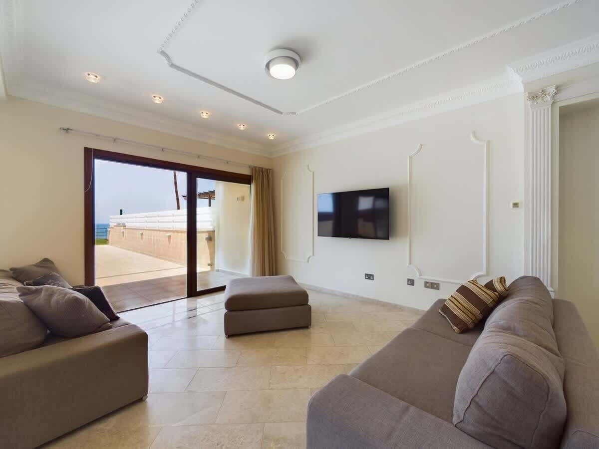 Een woonkamer met een bank, een voetenbankje en een flatscreen televisie aan de muur.