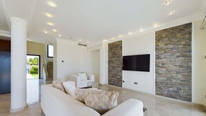 Ett rymligt vardagsrum med en stor vit soffa, en platt-TV som är monterad på en vägg av sten och en trappa som leder till ett annat plan.