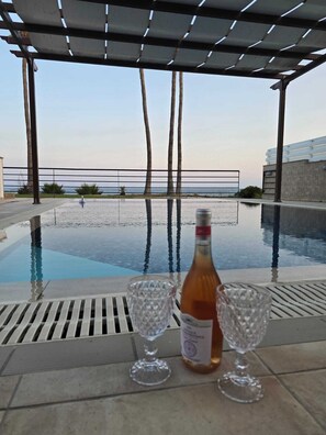 A poolside area with a bottle and two glasses, overlooking a beach with palm trees and a clear sky. - Fabulous Beach Front House (Perivolia)