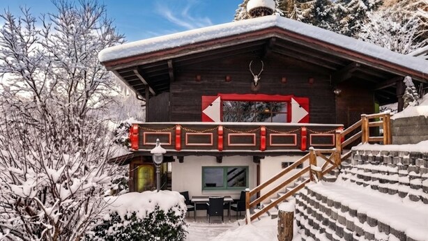 Eine Holzhütte mit einem rot-weißen Schild, einer Treppe und verschneiter Umgebung.