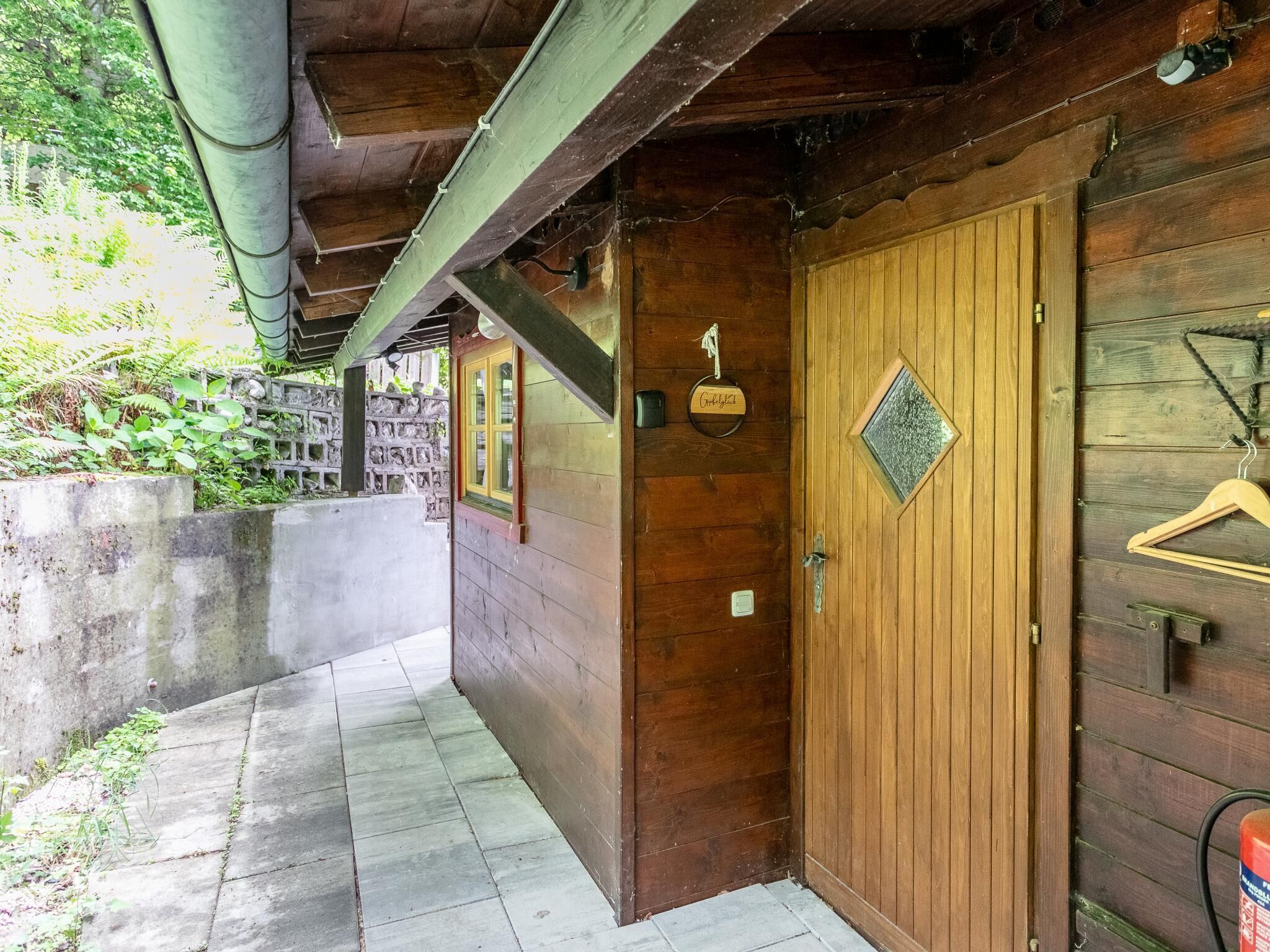 Una porta in legno con un piccolo oblò, un attaccapanni appeso e una parete in cemento con una finestra.