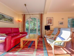 A living room with a red sofa, a wooden coffee table, and two lounge chairs. - Luxury detached home with garden and sauna (Brandscheid)