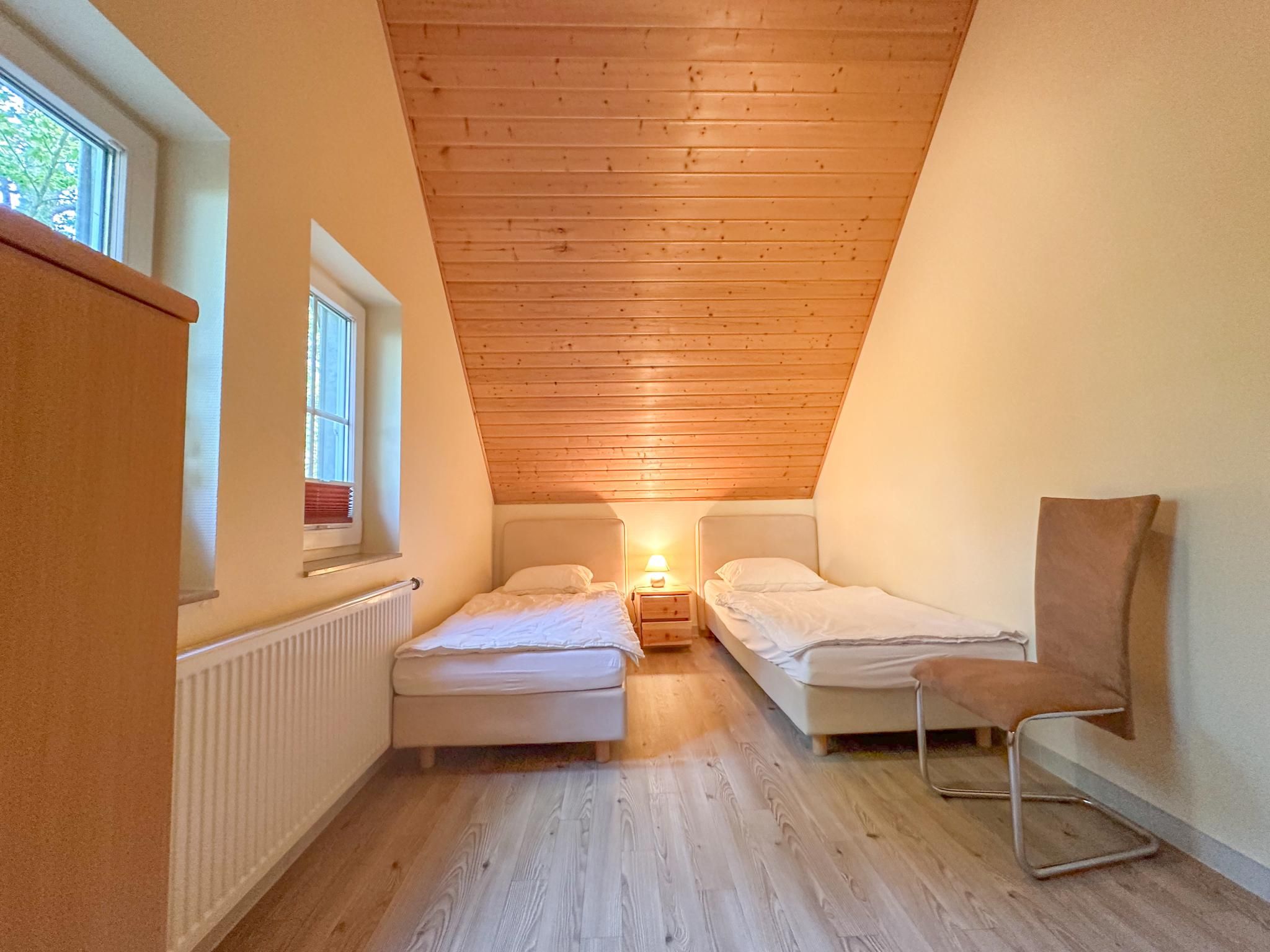 A small, cozy room with two beds, a chair, and a window.