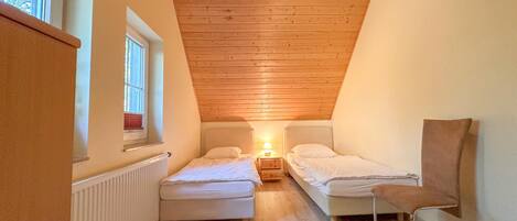 A small, cozy room with two beds, a chair, and a window.