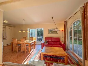 A spacious living area with a red sofa, wooden dining table, and chairs. There is a large window providing a view of the outdoors. - Luxury detached home with garden and sauna (Brandscheid)