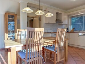 A dining area with a wooden table and chairs, a kitchen in the background, and pendant lighting. - Luxury detached home with garden and sauna (Brandscheid)