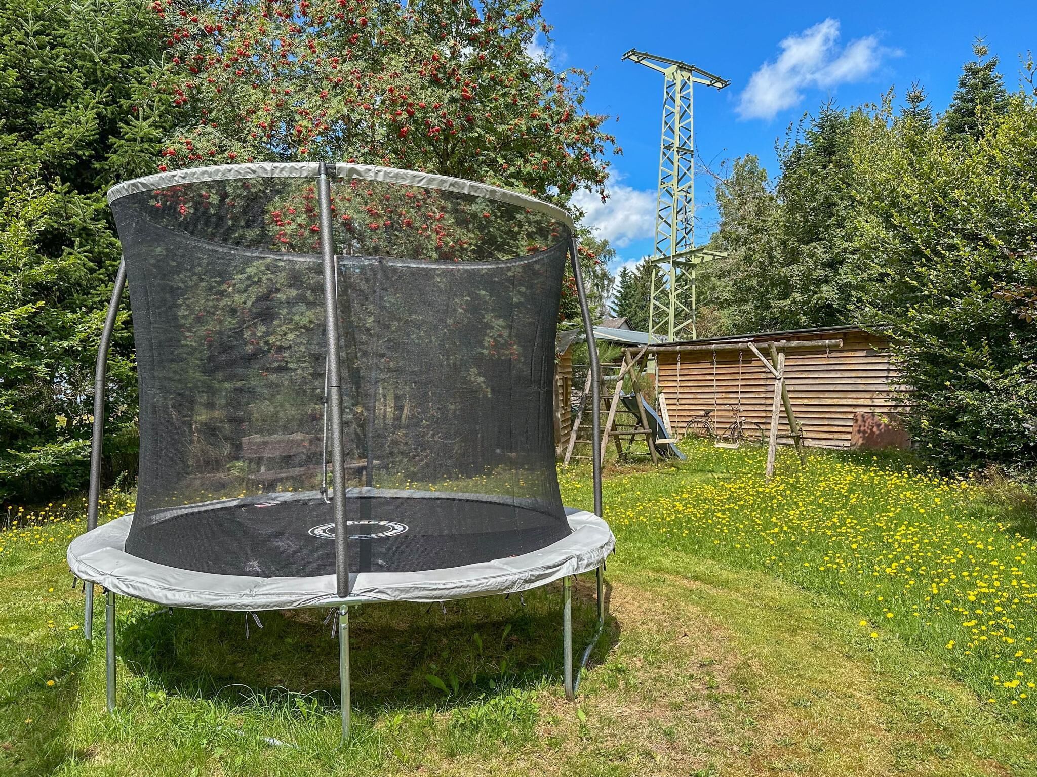 A trampoline in a grassy area with a wooden structure and a tall metal tower in the background.