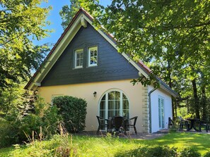 Ein Haus mit Satteldach, einer Garage und einer Terrasse mit Gartenmöbeln.