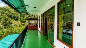 A balcony with a green floor, wooden cabinets, and large windows overlooking a lush green landscape. - Serenity Cottage (Ella)