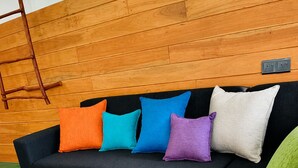 A sectional sofa with multiple cushions in various colors, a wooden wall, and a green carpet. - Serenity Cottage (Ella)