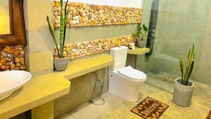 A bathroom with a stone wall, a sink, a toilet, a shower, and potted plants. - Serenity Cottage (Ella)
