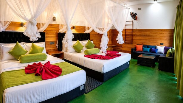 A hotel room with two beds, a sofa, a TV, and a mosquito net. - Serenity Cottage (Ella)