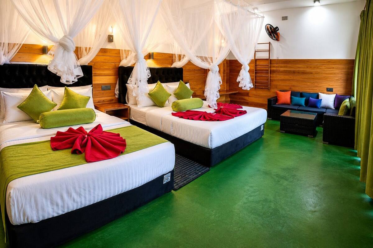 A hotel room with two beds, a sofa, a TV, and a mosquito net.