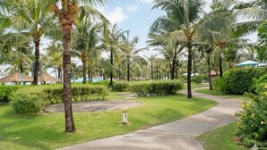 Un sendero bordeado de palmeras y una zona verde, que conduce a un edificio con techo de paja.