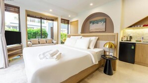 Una habitación de hotel con una cama grande, televisión, escritorio con lámpara y kitchenette.