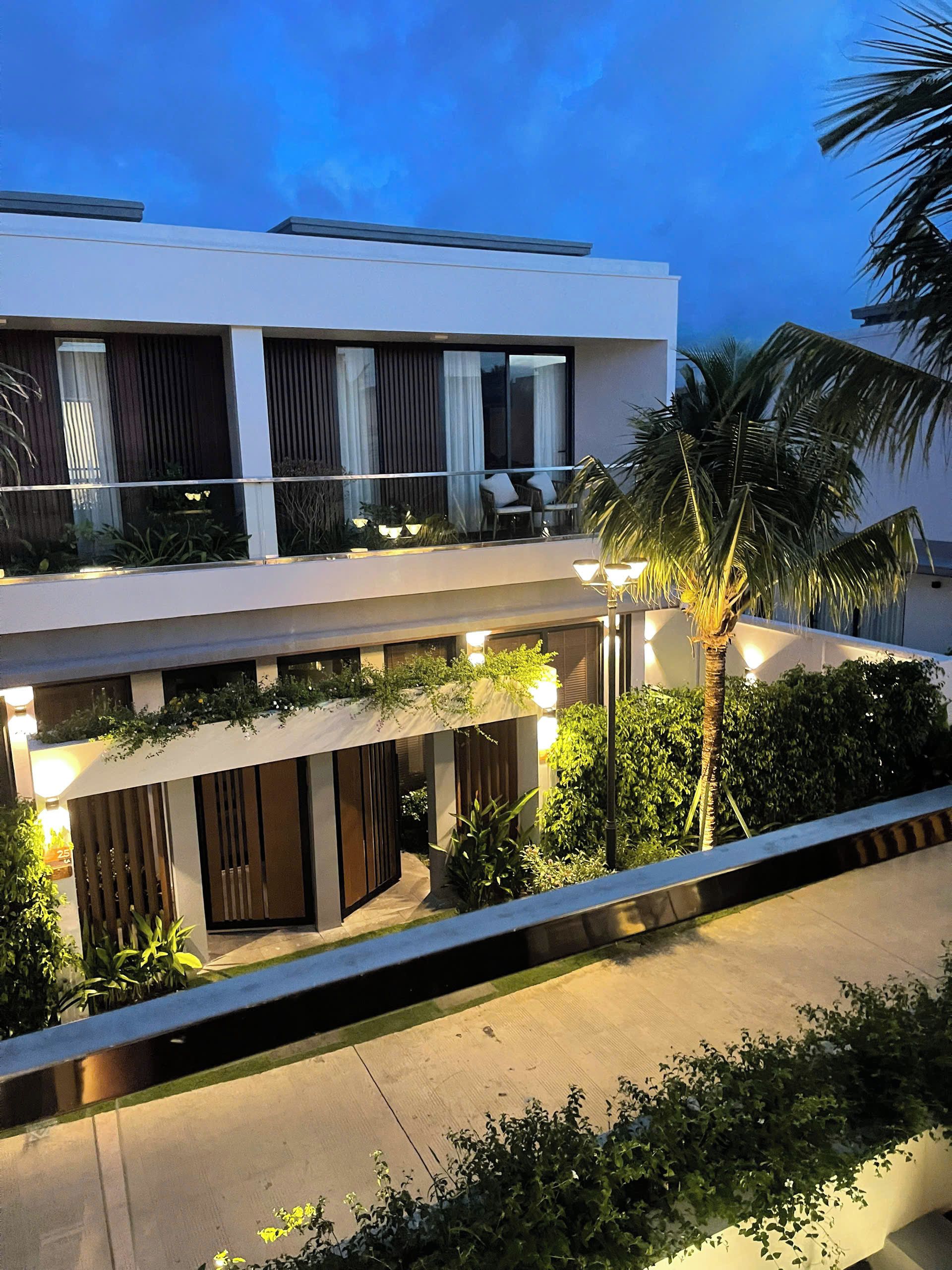 Un edificio moderno de dos pisos con balcón, mobiliario exterior y abundante vegetación.