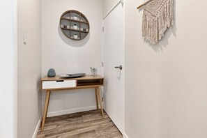 A hallway with a wooden desk, a round wall shelf with plants, and a macramé wall hanging. - Lake View Apartment with parking (Hamilton)