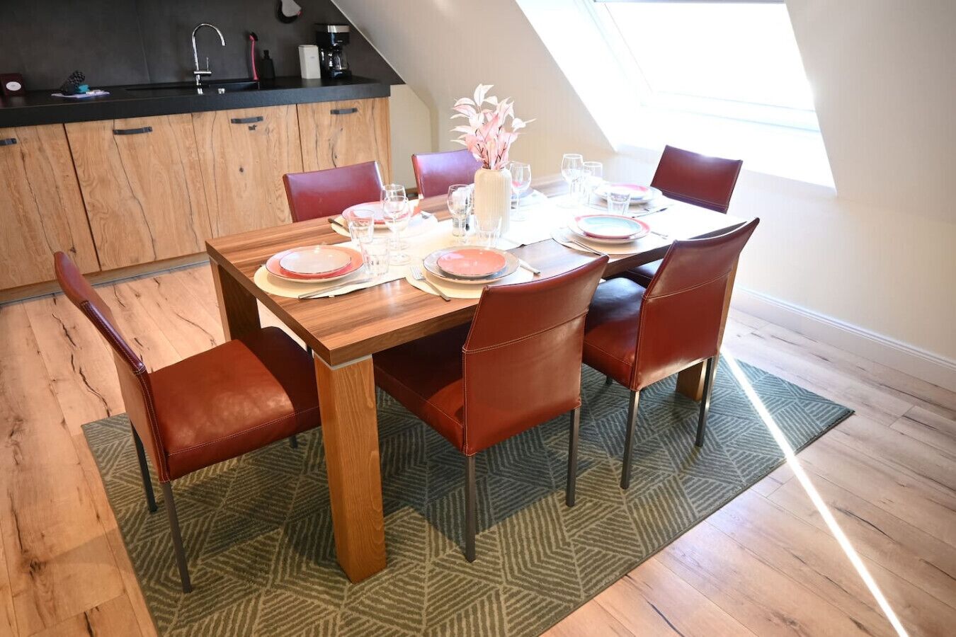 A dining area with a wooden table, red chairs, and a kitchen in the background.