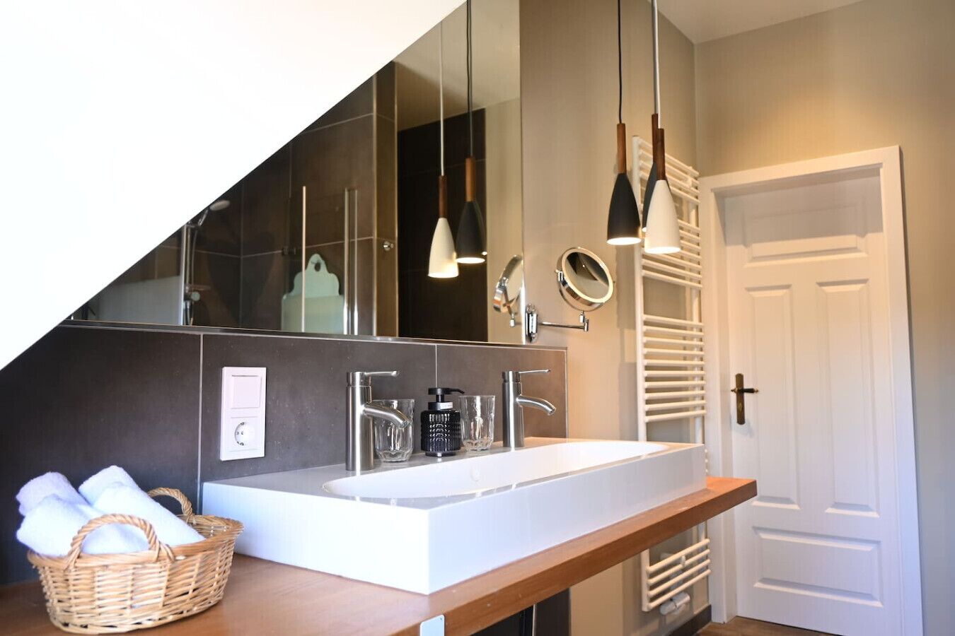 A modern bathroom with a large mirror, a white sink, and a wooden vanity.