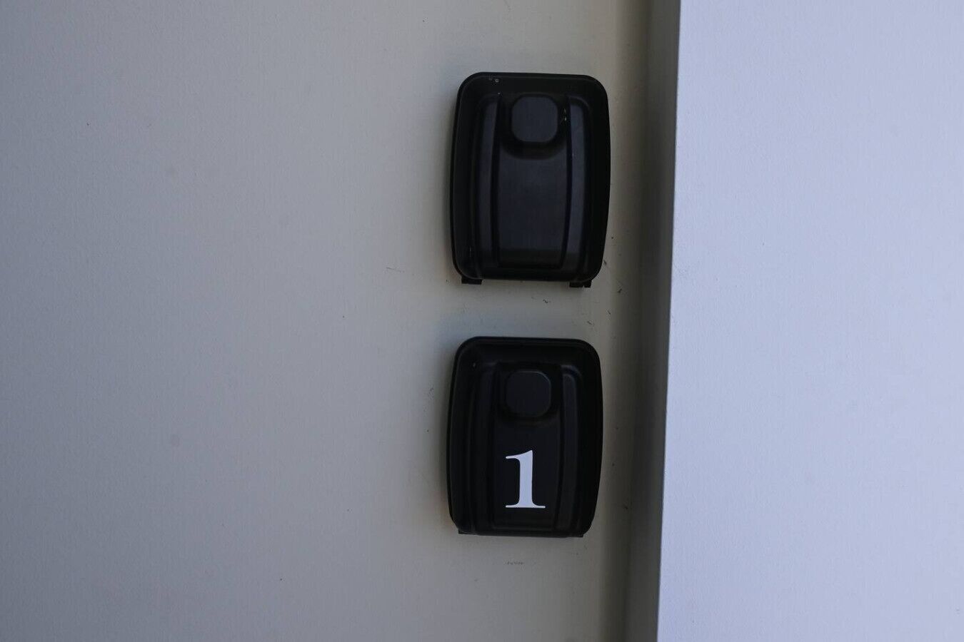 Deux objets noirs sur un mur, dont l’un porte le chiffre « 1 » en blanc.