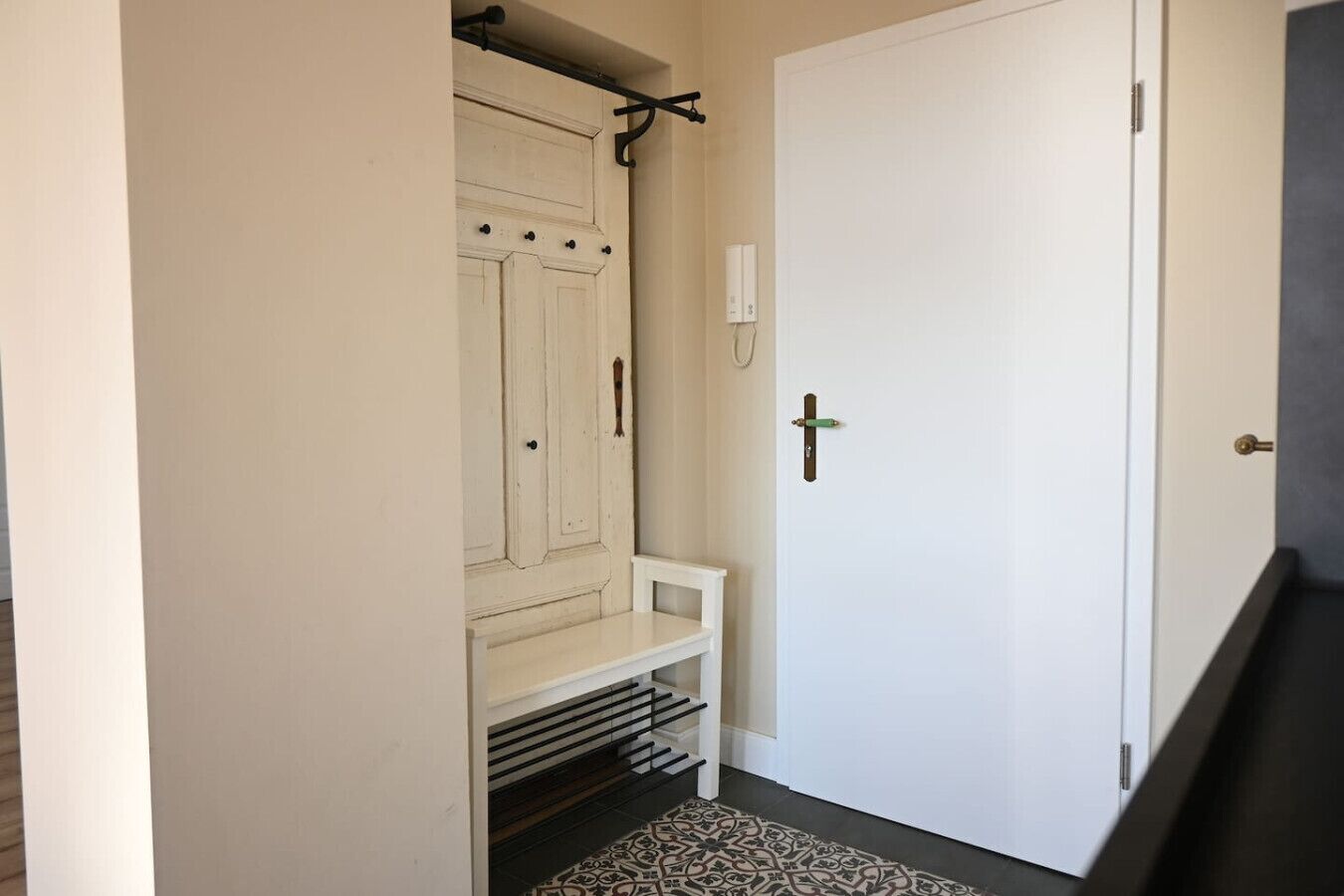 Un corridoio con una porta bianca, una panca e un tappeto decorato.