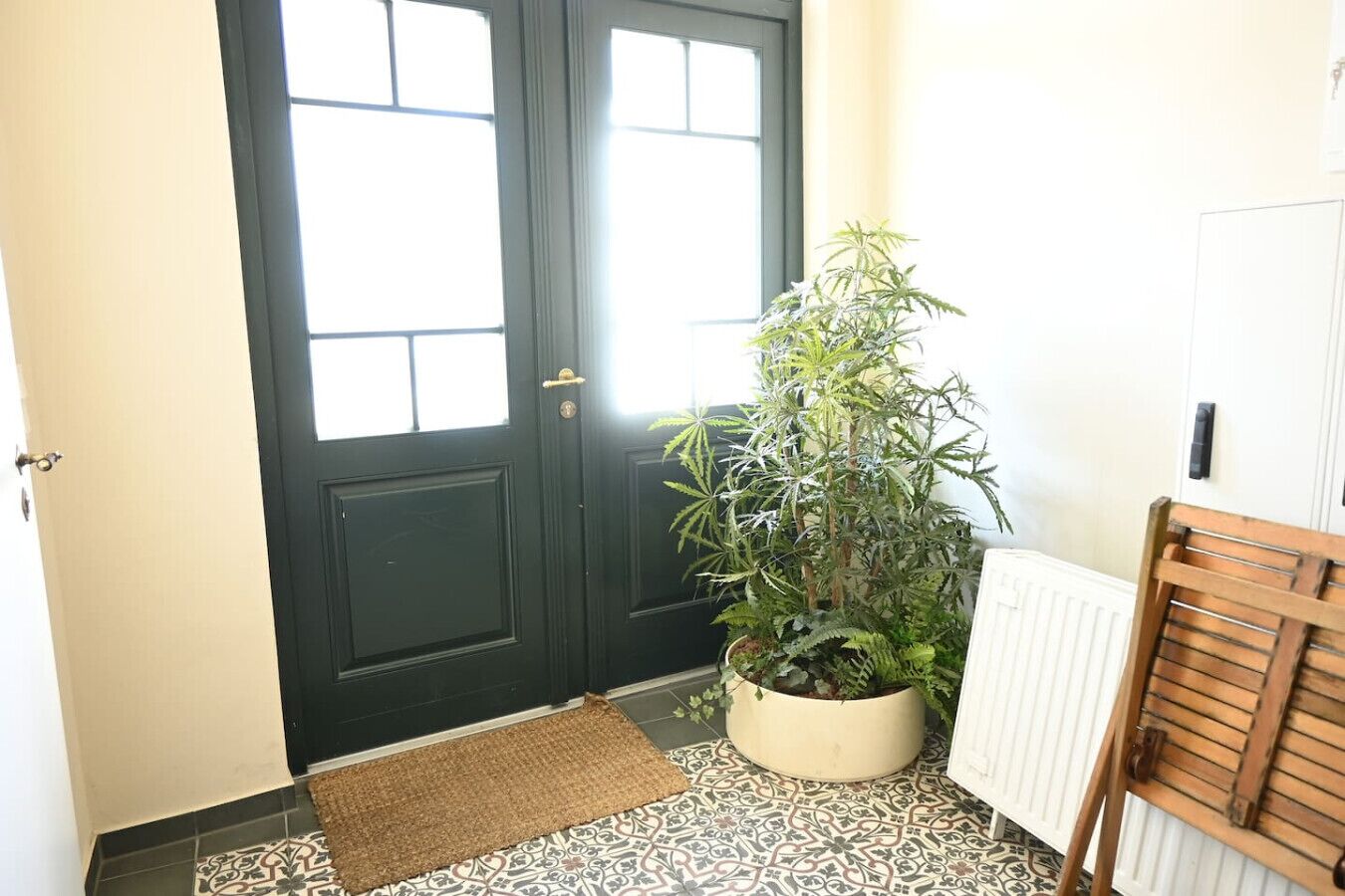 A black door with a window, a potted plant, a wooden bench, and a radiator.