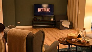 Un soggiorno con una televisione che mostra 'NETFLIX', un divano, un tavolino da caffè con degli snack e una parete di colore scuro.