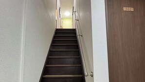 Eine Treppe mit hölzernem Geländer, einer Tür mit der Beschriftung '102' und einer Lampe am oberen Ende.