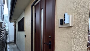 Ein schmaler Gang mit einer Holztür, einem Sicherheitstastaturfeld und einem an der Wand montierten Gegensprechanlage.