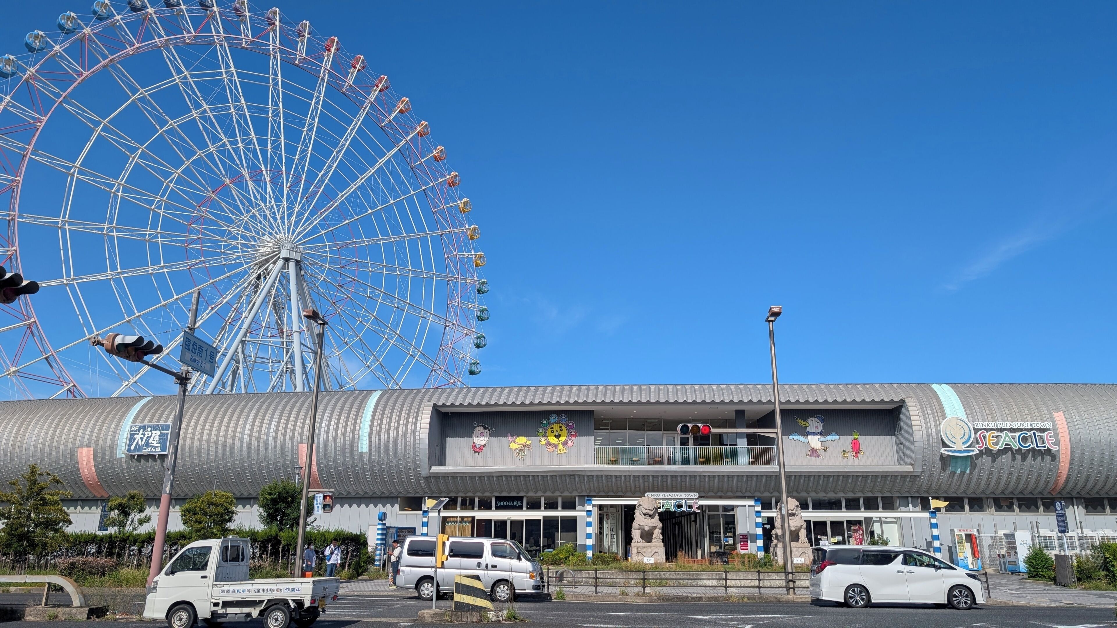 A building with a curved facade, a Ferris wheel in the background, and a statue in front.