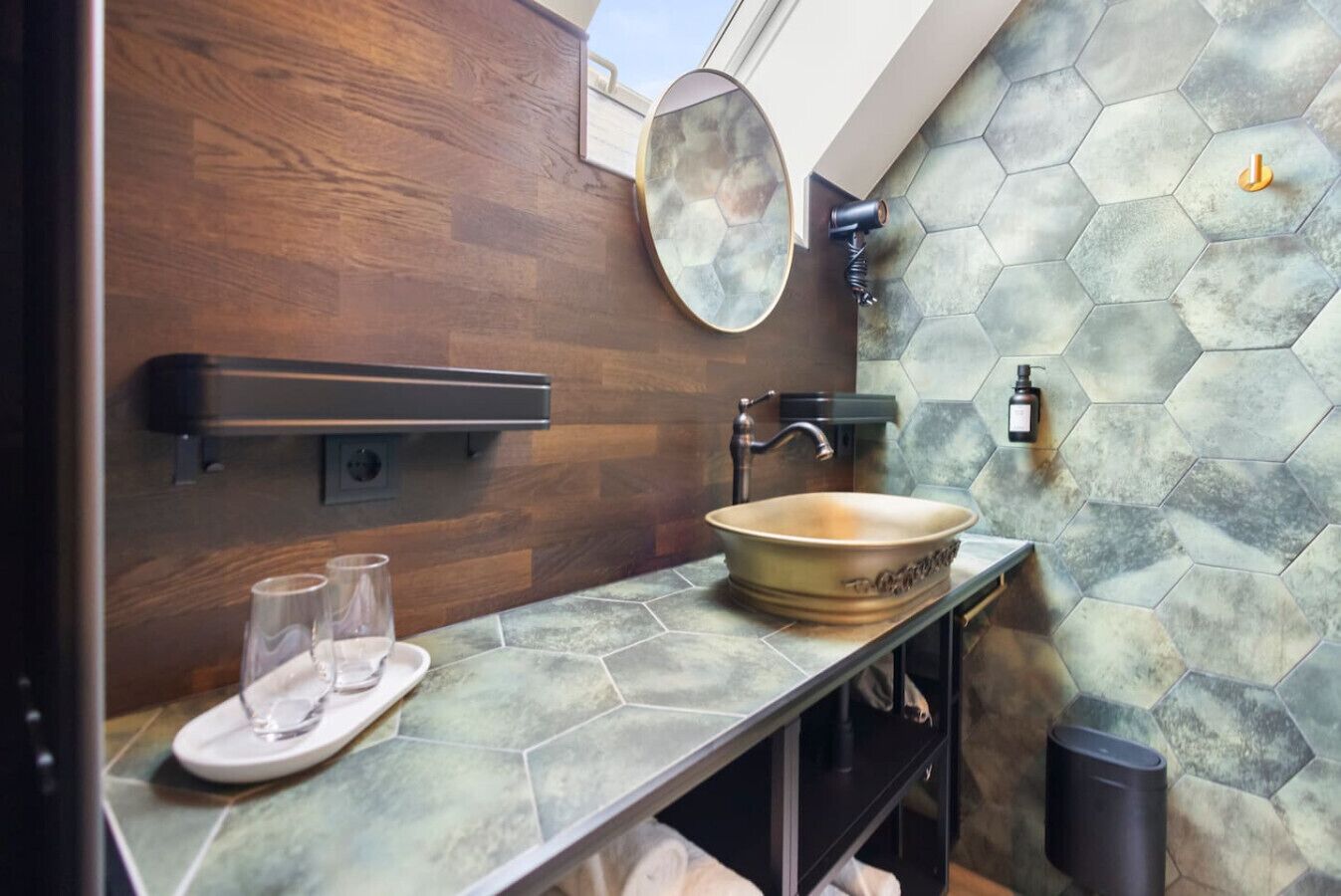 A bathroom with a wooden wall, a hexagonal tile backsplash, a round mirror, a vessel sink, and a towel rack.