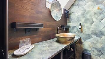 A bathroom with a wooden wall, a hexagonal tile backsplash, a round mirror, a vessel sink, and a towel rack.